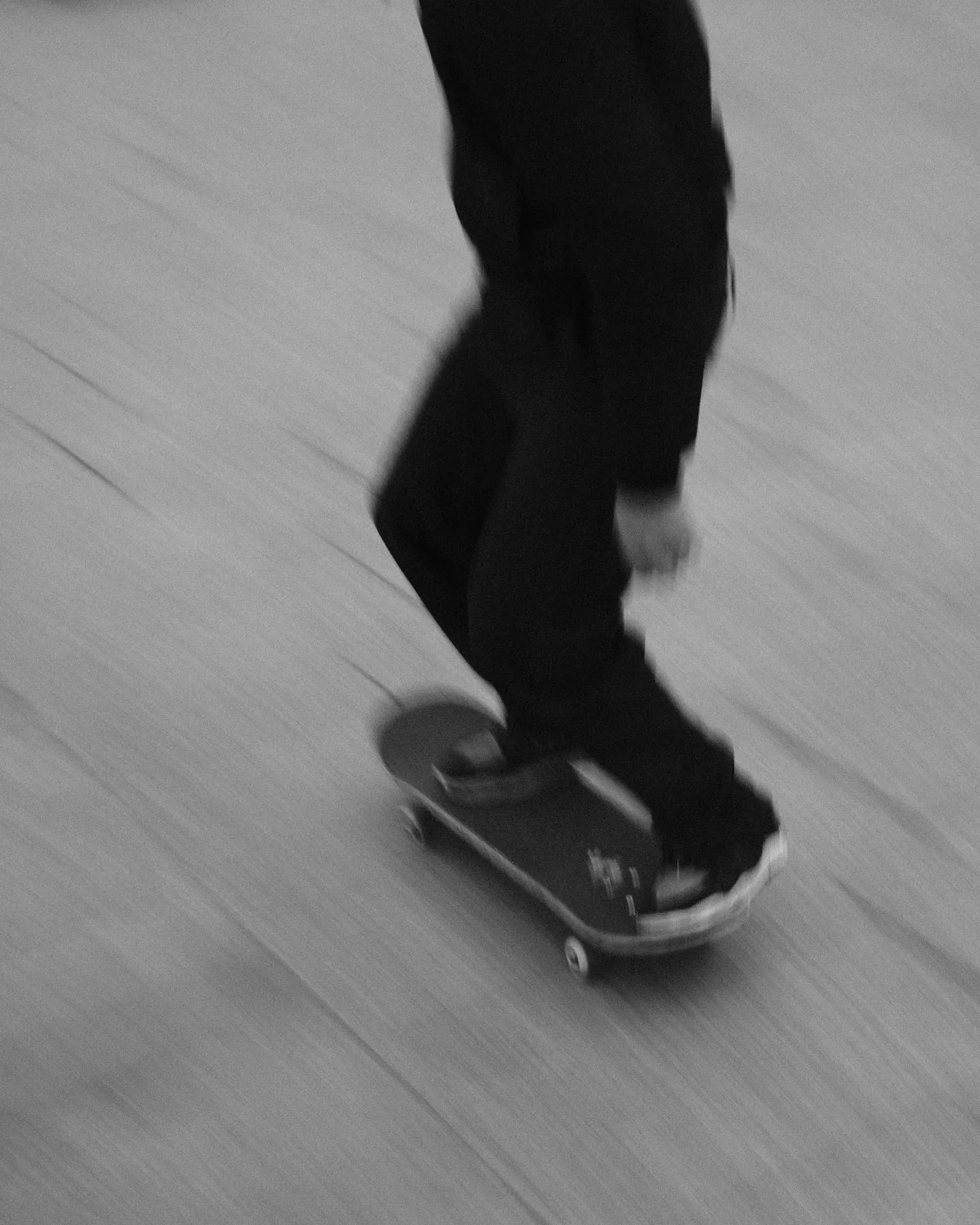 Panned black and white shot of a skateboarder, ground streaked by motion and heavy grain