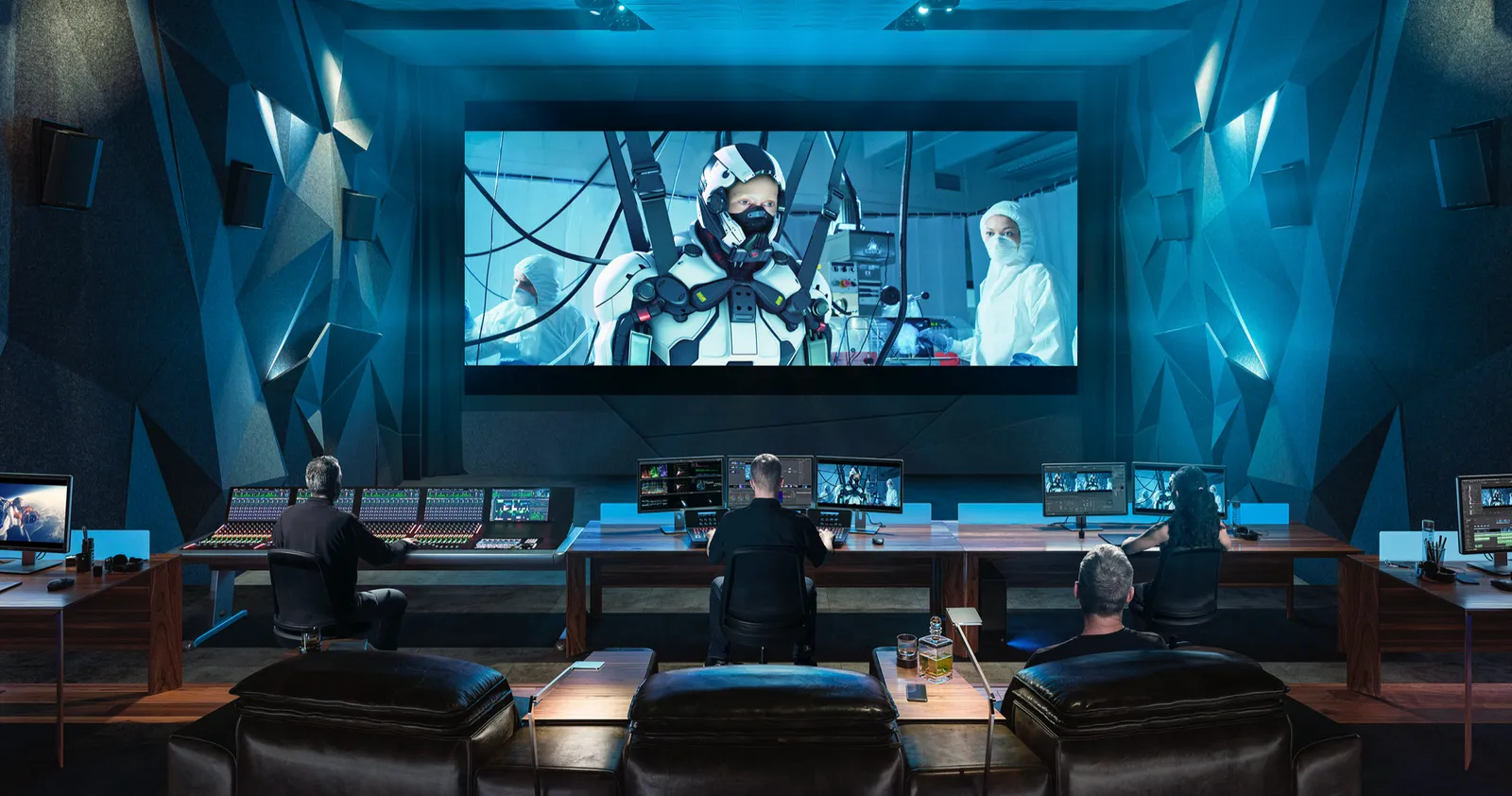 Three colourists at consoles in a professional grading theatre, facing a large cinema screen showing a sci-fi shot