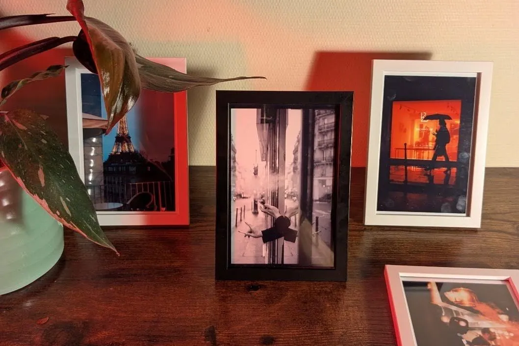 Framed 4x6 Selphy prints of Paris street scenes standing on a wooden shelf beside a houseplant