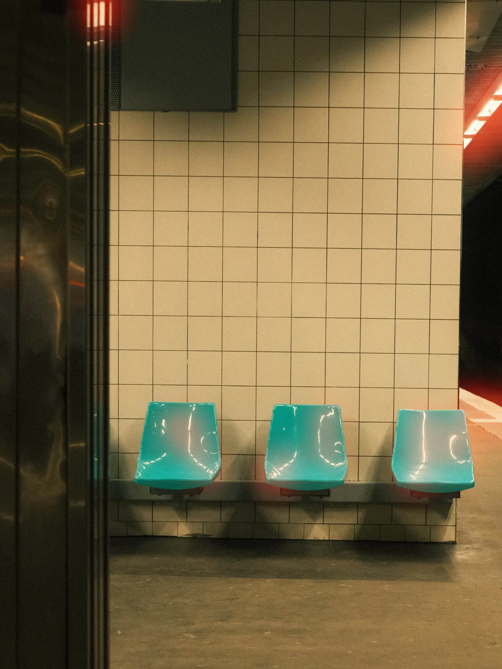 Warm red glow spreading from platform lights across a tiled metro station wall